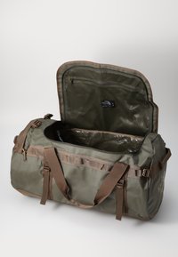 Olive green duffel bag with a top zip opening, fabric webbing, inner mesh pocket, and sturdy brown straps. Textured, durable material.