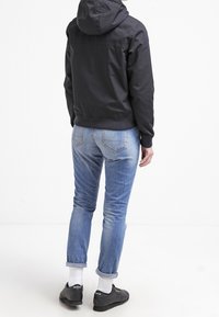 Svart huva jacka med dragkedja, kombinerad med ljusblå jeans och svarta sneakers. Jeansarna har uppvikt nederkant och bakfickor.