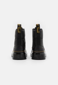 Bottines noires à cheville avec une finition en cuir lisse, semelles en caoutchouc nervurées, marquage jaune sur les languettes de tirage, et détails de surpiqûres contrastées.