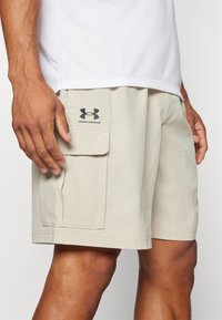Beige cargoshorts med sidficka och Under Armour-logotyp. Tillverkade av lättviktsmaterial, med rak passform och sydda kanter.