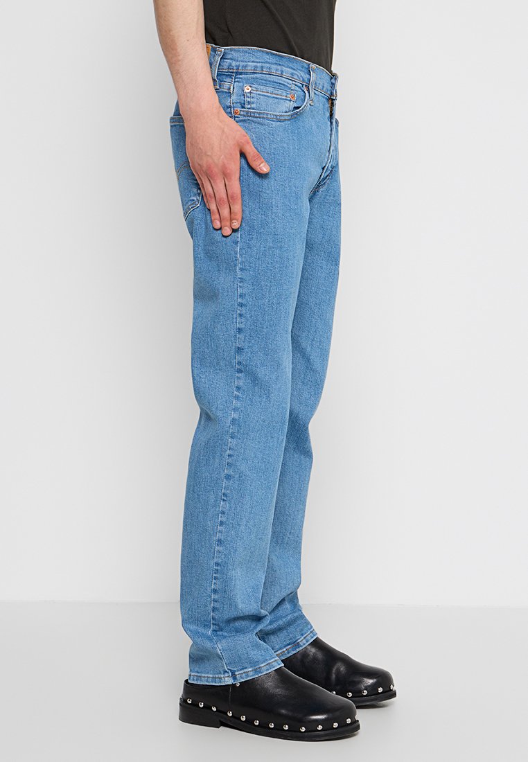 Jeans droits en denim bleu clair avec cinq poches, une taille ajustée et des coutures contrastées. Portés avec des sabots noirs ornés d'accents cloutés.