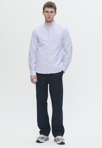 Light blue striped button-up shirt with a collar, paired with dark navy trousers and gray sneakers. Clean design, no patterns or accents.