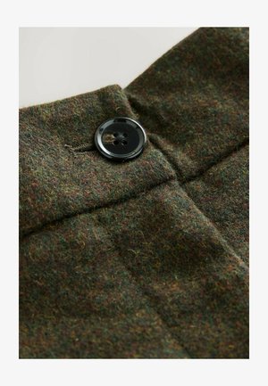 Tweed fabric in dark green with subtle flecks of red and yellow. Features a prominent black four-hole button and neat stitching.