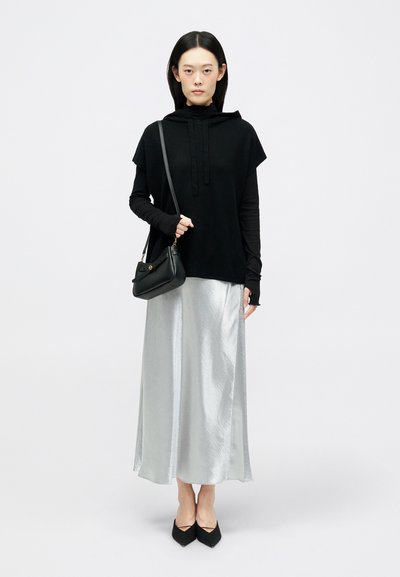 Μαύρη κουκούλα πάνω από μια μακριά ασημένια σατέν φούστα, συνδυασμένη με μαύρες μυτερές μπαλαρίνες. Μια μικρή μαύρη τσάντα χιαστί φοριέται στον ώμο.