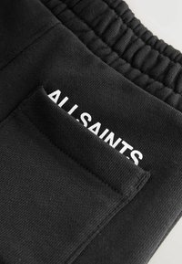 Melni treniņbikses, kas izgatavotas no mīksta auduma, ar elastīgu jostu. Aizmugurē ir kabata ar baltiem burtiem "ALLSAINTS".