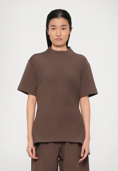 Brown short-sleeved top with a high neck. Features a smooth texture and loose fit. Paired with matching brown trousers for a cohesive look.