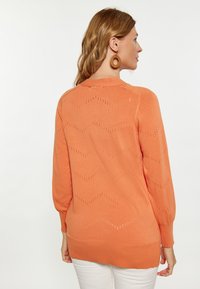 Maglione lavorato a maglia arancione con motivo a zigzag, maniche lunghe e polsini a coste. Leggero, con dettagli a foro aperto lungo il design.