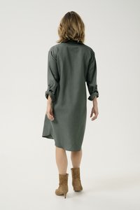 Lang groen hemdjurk met opgerolde mouwen, knoopaccenten en een relaxte pasvorm. Gecombineerd met middelhoge tan suede enkellaarsjes.