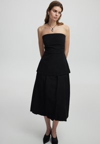 Schwarzes trägerloses Kleid mit tailliertem Oberteil und Peplum-Taille, kombiniert mit einem fließenden, knöchellangen Rock. Glatte Stoffstruktur.