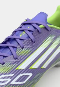 Purple soccer cleat featuring a textured finish, green accents, and white stripes, with a lace-up design and curved silhouette.