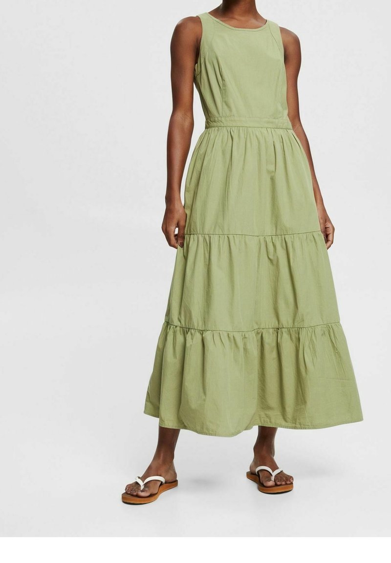 Robe maxi en coton vert avec un design sans manches, taille froncée et jupe à volants. Elle présente une texture lisse et un col rond simple.