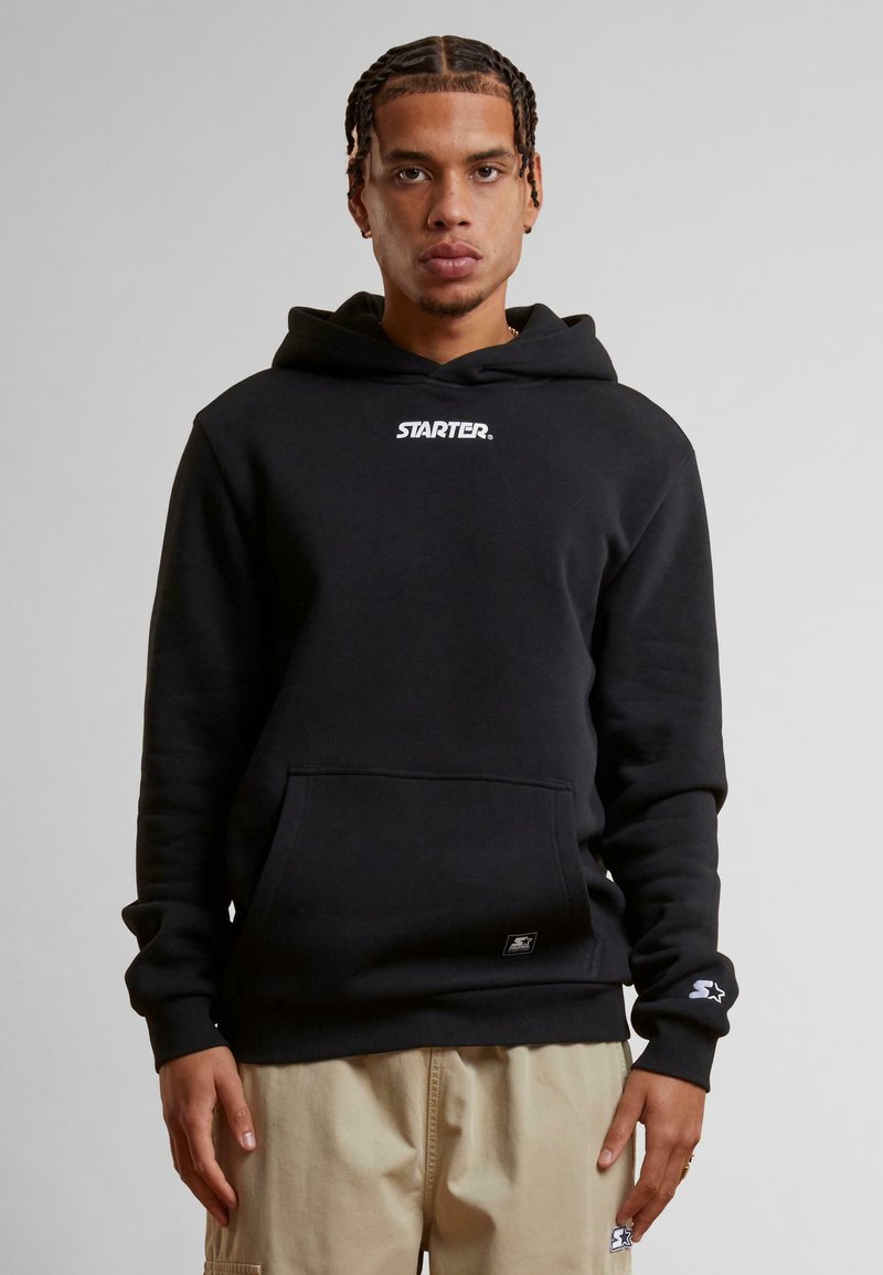 Sweatshirt à capuche noir avec poche frontale, arborant un logo "STARTER." blanc et un tissu texturé. Manches longues avec accents de poignet.