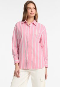 Camicia button-up rosa chiaro con strisce verticali bianche e blu, con colletto e logo ricamato sul petto. Tessuto morbido.