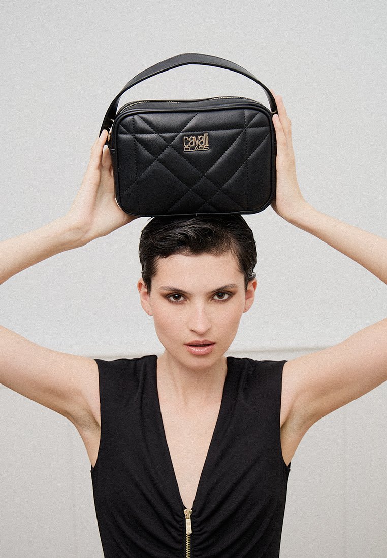 Bolso acolchado negro con un asa superior, que presenta un detalle del logo dorado. Material suave con una forma cuadrada y un patrón de costura prominente.