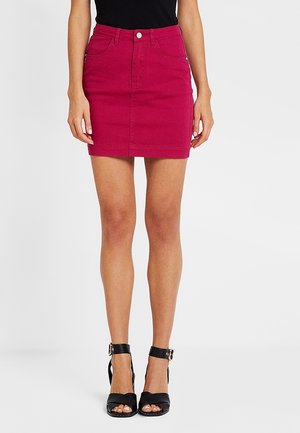 Dopasowana spódnica dżinsowa w jaskrawym fuksjowym kolorze z pięcioma kieszeniami, zapięciem na guziki z przodu i prostym krojem, zestawiona z czarnymi sandałami na wysokim obcasie.