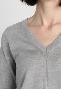 Šedý svetr s výstřihem do V vyrobený z měkkého, lehkého materiálu s jemným prošíváním kolem výstřihu a se uvolněným střihem.