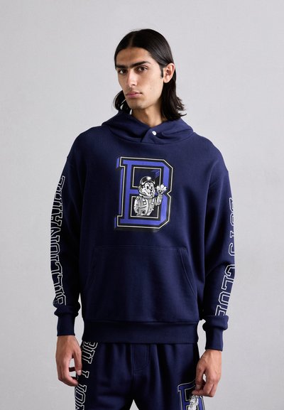 Granatowy hoodie wykonany z miękkiego materiału, z graficznym nadrukiem postaci i literą 'D' z przodu; długie rękawy z napisem po bokach.