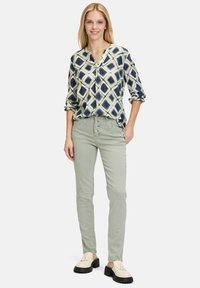 Chemise à manches longues à motif géométrique bleu et crème, assortie avec un pantalon ajusté vert clair à devant boutonné. Porté avec des chaussures de couleur claire.