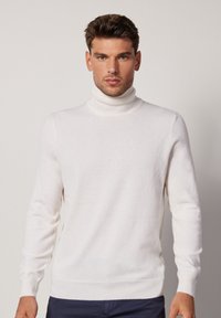 Maglione a collo alto bianco realizzato in morbido tessuto a maglia. Presenta maniche lunghe e un design aderente, con una texture liscia e polsini a coste.