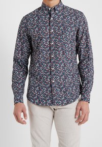 Camicia button-up con sfondo blu scuro e piccolo motivo floreale in rosso, bianco e verde. Presenta un colletto classico e maniche lunghe.