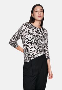 Black and white printed long-sleeve top featuring animal and graphic patterns, crew neckline, and relaxed fit, paired with black trousers.