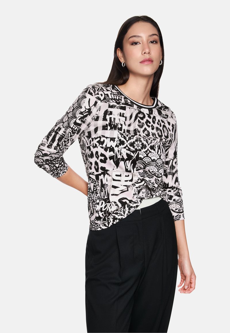 Black and white printed long-sleeve top featuring animal and graphic patterns, crew neckline, and relaxed fit, paired with black trousers.