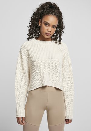 Chunky stickad krämfärgad tröja med en kortad design, bred ribbad textur och rundad halsringning. Kombinerad med beige leggings.