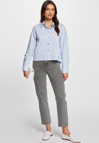 Lichtblauwe button-up overhemd met lange mouwen, voorzien van een puntige kraag. Gecombineerd met grijze rechte jeans en witte instappers.