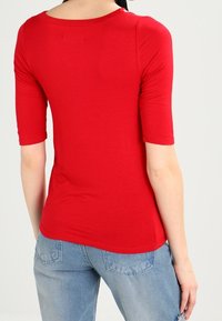Camisa roja de manga corta con cuello redondo. Hecha de una tela suave y elástica. Presenta un diseño ajustado y un detalle de costura en la parte posterior.