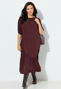 Bordeaux midi-jurk met korte mouwen, geplooide halslijn en zijplooien. Gediend met bruine kniehoge laarzen en een gestructureerde handtas.