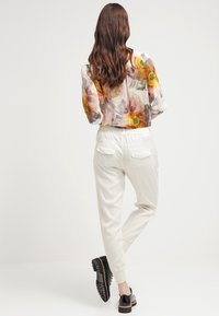 Vita joggerbyxor med elastisk midja, smalnade ben och bakfickor. Modellen bär en genomskinlig blommig blus och svarta snörskor.