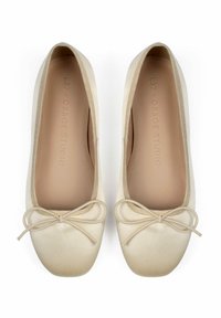 Ballerines en satin beige avec un bout rond, un accent en nœud et une texture douce et lisse. Contient un logo sur la semelle intérieure.