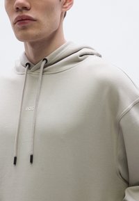 Helebeeži kapuutsiga pusa, mis on valmistatud pehmest kangast, millel on paelaga kapuuts, tikitud "BOSS" logo ja minimalistlik disain ilma nähtavate mustriteta.