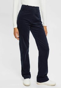 Morskie spodnie z kordurojowej tkaniny, z wysokim stanem, szerokimi nogawkami, przednimi kieszeniami i zapięciem na guzik. Połączone z białymi trampkami.