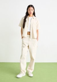 Cream striped short-sleeve shirt and matching pants, both in a light fabric. White sneakers with lace-up closure complete the outfit.