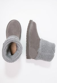 Par de botas de invierno de ante gris con puños de punto plegables, mostradas desde vistas superiores y laterales sobre un fondo blanco.