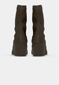 Bottes en suède marron, à la cheville, avec un design loose, un talon haut en bloc et des coutures visibles le long de la couture arrière.