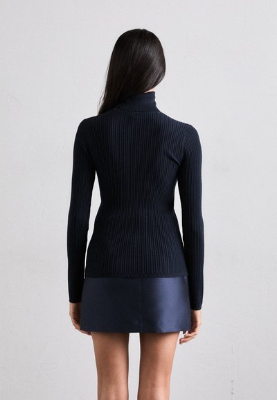 Marineblå ribbet high neck sweater med lange ærmer, tætsiddende design og en glat tekstur, parret med en mørk, skinnende mini nederdel.
