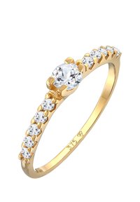 Anello d'oro con una pietra centrale trasparente e sei pietre più piccole lungo la fascia, che presenta una finitura lucida e impostazioni a corona.