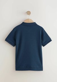 Dunkelblaues kurzärmliges Poloshirt, das an einem Holzkleiderbügel hängt. Es hat einen gerippten Kragen und Bündchen sowie eine glatte Baumwolltextur.