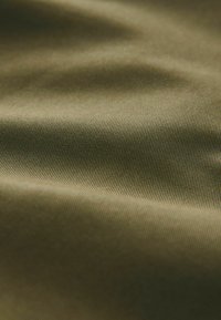 Tissu vert olive lisse avec une fine texture nervurée diagonale et des plis doux créant des ombres délicates.