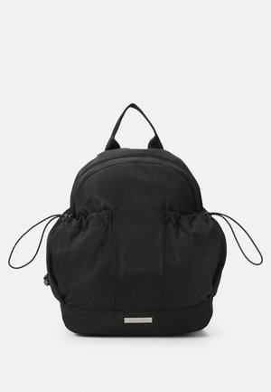 Mochila negra hecha de nylon suave, con forma redondeada, dos bolsillos laterales elásticos y un asa en la parte superior. Cierre de cremallera en la parte superior.