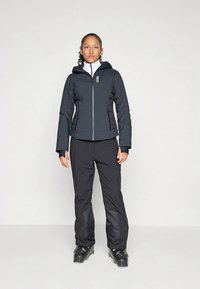 Mustast veekindlast kangast kapuutsiga jope, esiluku ja kehale kohandatud lõikega, mis on kokku sobitatud mustade pükstega. Mõlemad on valmistatud tekstureeritud, vastupidavast kangast.