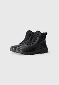 Bottines en cuir noir avec semelles épaisses, fermetures éclair latérales et lacets sur un fond blanc uni.