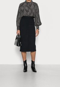 Musta kynähame yhdistettynä kuvioituun paitapuseroon. Paitapuserossa on puffeja hihoja. Mustat nilkkurit ja teksturoitu musta käsilaukku täydentävät asun.