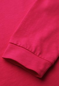 Jasnoróżowy, długi rękaw, z ribbowanym mankietem. Tkanina wydaje się gładka, z lekkim połyskiem i subtelną teksturą.