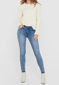 Helle Cremefarbe Sweater, kombiniert mit hellblauen Slim-Fit-Jeans. Die Jeans haben ein klassisches Fünf-Taschen-Design und werden von weißen Ankle Boots ergänzt.