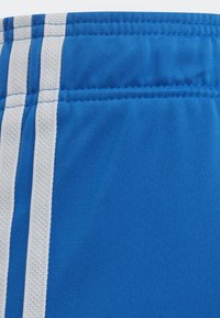 Modré sportovní šortky vyrobené z měkké tkaniny, s třemi vertikálními bílými pruhy po stranách a jednoduchým elastickým pasem.