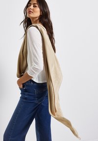 Beige sjaal over een wit overhemd met lange mouwen, met gedetailleerde textuur en subtiele patronen, gecombineerd met blauwe spijkerbroek.