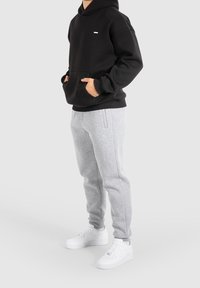 Černá mikina s kapucí a přední kapsou, malý emblém, jako doplněk světle šedé tepláky a bílé tenisky. Pohodlný střih a měkká textura.